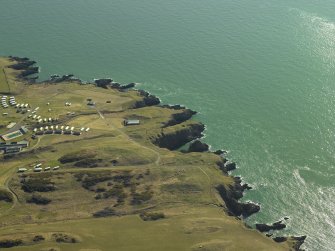 Oblique aerial view centred on the remains of the promontory fort, tower-house, anti-aircraft battery, buildings and huts, taken from the NW.