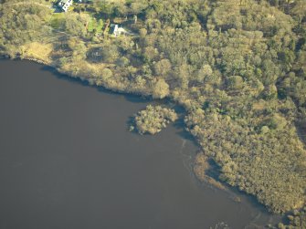 Oblique aerial view centred on the remains of the crannog with the remains of the castle, and the cottage and offices adjacent, taken from the W.