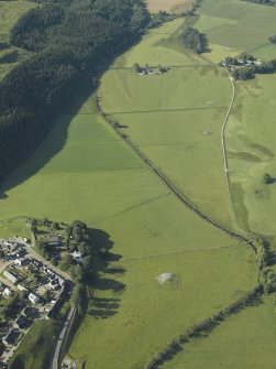 Oblique aerial view centred on the church, churchyard, burial-ground and museum with the remains of the cairns adjacent, taken from the N.