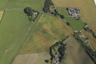 Oblique aerial view centred on the cropmarks of the enclosures and possible building with the manse, farmsteading, farmhouse and remains of the abbey adjacent, taken from the W.
