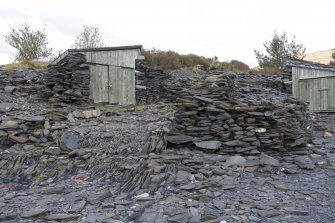 Detail from NE.  Showing modern wooden huts built into slate heaps.