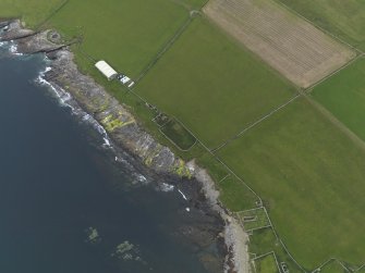Oblique aerial view of the remains of the brochs, settlement, church, hall, tower house and shed covering the chambered cairn, taken from the S.