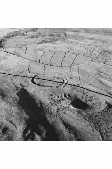 Oblique aerial view of Kirk Hill centred on the remains of a fort and palisaded enclosure with buildings, enclosures, lazy-beds, quarries and a farmstead, field-system, rig and boundary bank adjacent, taken from the WNW.