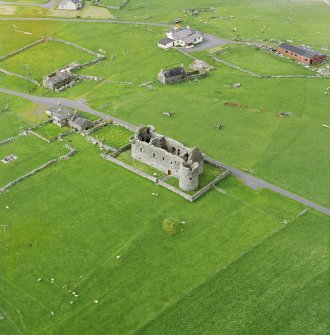 Oblique aerial view centred on the remains of Muness Castle with a mound adjacent, taken from the South.