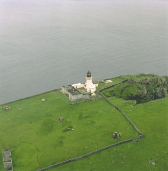 Oblique aerial view centred on the lighthouse with the remains of the dun adjacent, taken from the NNE .