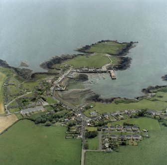 Oblique aerial view centred on the village with the remains of the promontory fort and chapel adjacent, taken from the NW.
