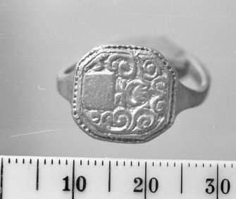 Gold finger ring with a blank field set within an engraved foliate design. The blank field was presumably intended to contain the initials of the purchaser.  Scale in millimetres.