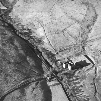 Oblique aerial view of Hermitage Castle centred on the remains of a castle with a chapel, boundary dyke and moated site adjacent, taken from the ESE.