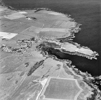 Oblique aerial view, taken from the SW, centred on the village and harbour, and showing Isle Head fort and the remains of St. Ninian's Chapel in the centre right of the photograph.