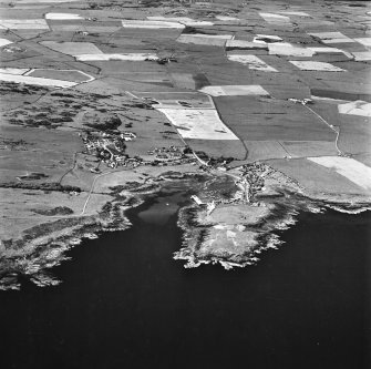 Oblique aerial view, taken from the S, centred on the village and harbour, Isle Head fort and the remains of St. Ninian's Chapel.