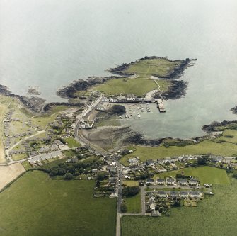 Oblique aerial view centred on the village with the remains of the promontory fort and chapel adjacent, taken from the NW.