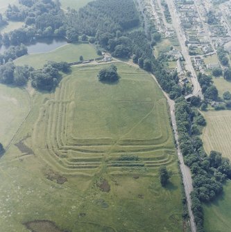 Oblique aerial view centred on the remains of the Roman Fort, chapel and burial ground, with road bridge adjacent, taken from the NNE.