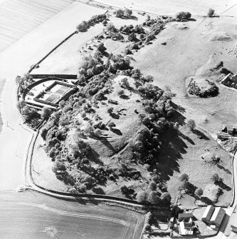 Oblique aerial view centred on the remains of the vitrified fort and broch with the house, walled garden and lodge adjacent, taken from the NE.