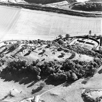 Oblique aerial view centred on the remains of the vitrified fort and broch with the house, walled garden and lodge adjacent, taken from the NW.
