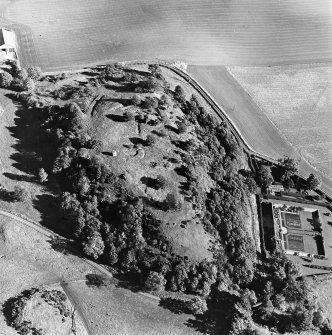 Oblique aerial view centred on the remains of the vitrified fort and broch with the house, walled garden and lodge adjacent, taken from the W.