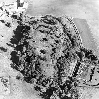 Oblique aerial view centred on the remains of the vitrified fort and broch with the house, walled garden and lodge adjacent, taken from the WSW.