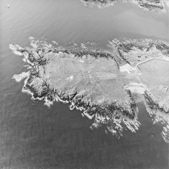 Oblique aerial view centred on the remains of the promontory fort with the remains of rig and the chapel adjacent, taken from the NE.