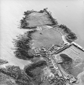 Oblique aerial view centred on the remains of the chapel with the remains of the promontory fort and the village adjacent, taken from the NNW.