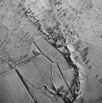 Oblique aerial view of Ettleton Sike centred on a burial ground with a building, field-system, rig and sheepfold and hut, field-system, rig and enclosure adjacent, taken from the SE.