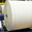 Interior. Foundry building. View of foam rubber underfloor being cut . A bale of rubber is rolled from one wheel to another and blades cut of a set thickness of underfloor coveringduring transfer from reel to reel.