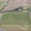Oblique aerial view of a circular cropmark, part of the First World War airship station gas works, and East Fortune farm, looking N.