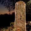 Artificially lit view of medieval graveslab in reuse as gatepost on S side of entrance, NY 2577 8019.