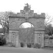 General view of arch, Culzean Castle, entrance gate with castellated top, roundels to side, a coat of arms and a sculpture of a putti riding a dolphin on the top.
