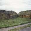 View of 2 barns, one with corrugated iron roof, one with thatched roof.