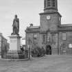 View from S of town hall and statue of Robert Bruce, High Street, Lochmaber. Large carts are balanced end on behind the statue.


