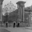View of three men in front of unidentified entrance gates with heraldic design and the date 1893