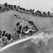 Oblique aerial view centred on the church, burial ground, farmsteading and barn with saltings adjacent, taken from the SW.