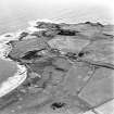 Oblique aerial view centred on the remains of the linear earthwork with farm, building and coastguard station adjacent, taken from the WNW.