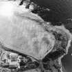 Oblique aerial view of Kinghornie centred on the cropmarks of possible graves with a house and farmsteading and cropmarks of round-houses, a possible souterrain, pits and a possible enclosure adjacent.  In addition, there are the remains of a pillbox and anti-tank blocks on the shore. Taken from the NW.