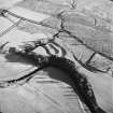 Oblique aerial view of Liddel Castle centred on the remains of an earthwork fortification with a burial ground and remains of a church adjacent, from NW.