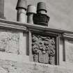 West front, armorial plaque surmounted by decorative chimney pot, detail