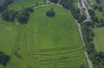 Oblique aerial view centred on the remains of the Roman Fort, chapel and burial ground, with road bridge adjacent, taken from the NE.