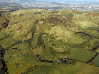 General oblique aerial view centred on the rifle ranges, farmhouse and farmsteading and the remains of the rig, fort, cultivation terraces and palisaded settlement, taken from the SE.