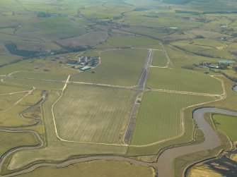 Oblique aerial view centred on the remains of the airfield and control tower with the sawmill adjacent, taken from the NE.