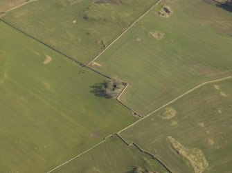 Oblique aerial view centred on the remains of the church and burial ground, taken from the W.