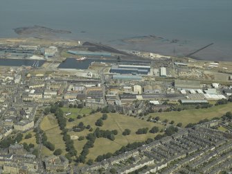 Oblique aerial view centred on the dock, dry dock and the railway station with Leith Links in the foreground, taken from the SW.