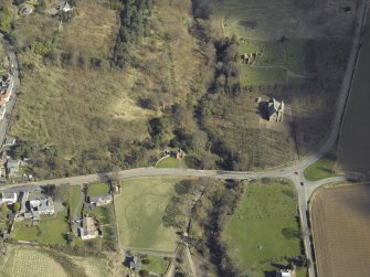 Oblique aerial view centred on the gate lodge, with the church, burial ground, war memorial and remains of the church adjacent, taken from the SW.