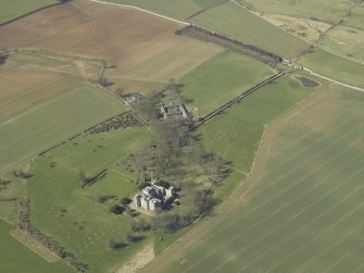 Oblique aerial view centred on the country house, stable block and landscaped gardens with the gate and gate lodge adjacent, taken from the ESE.
