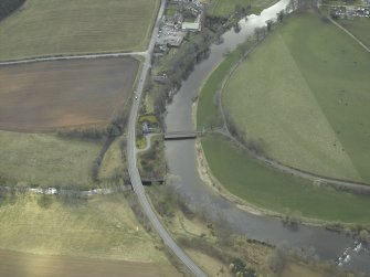 Oblique aerial view centred on the suspension bridge, farmhouse, farmsteading, cottage and road bridge, taken from the NE.
