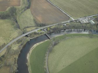 Oblique aerial view centred on the suspension bridge, farmhouse, farmsteading, cottage and road bridge, taken from the NW.