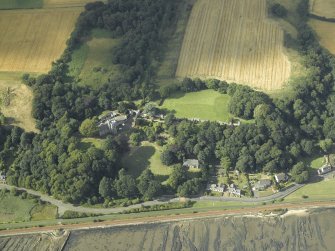 Oblique aerial view centred on the country house, cottage and church, taken from the SSE.