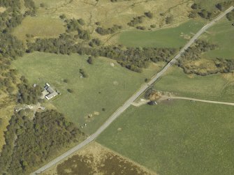 Oblique aerial view centred on the remains of the cairn with the building and enclosure adjacent, taken from the NW.