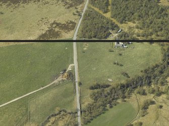 Oblique aerial view centred on the remains of the cairn with the building and enclosure adjacent, taken from the SE.