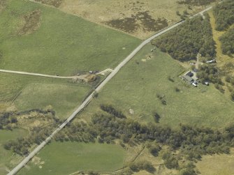Oblique aerial view centred on the remains of the cairn with the building and enclosure adjacent, taken from the E.