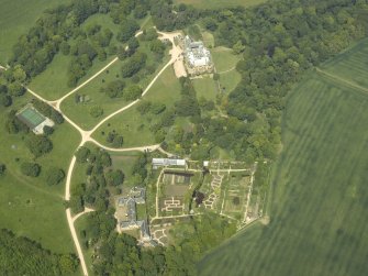 Oblique aerial view centred on the country house with the walled gardens and stables adjacent, taken from the S.