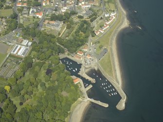 Oblique aerial view centred on the harbour with the monastery, garden, church, churchyard and burial ground adjacent, taken from the SW.